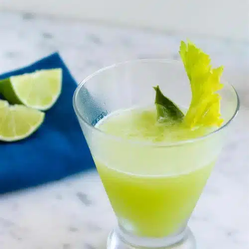 Cocktail in a footed glass on a blue napkin with lime wedges alongside