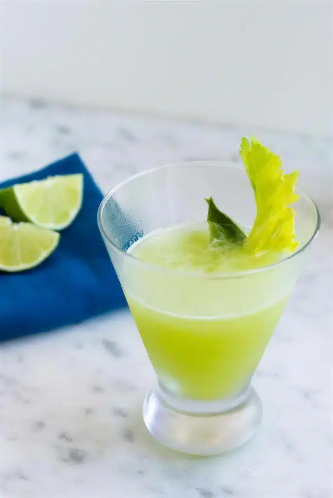 Cocktail in a footed glass on a blue napkin with lime wedges alongside