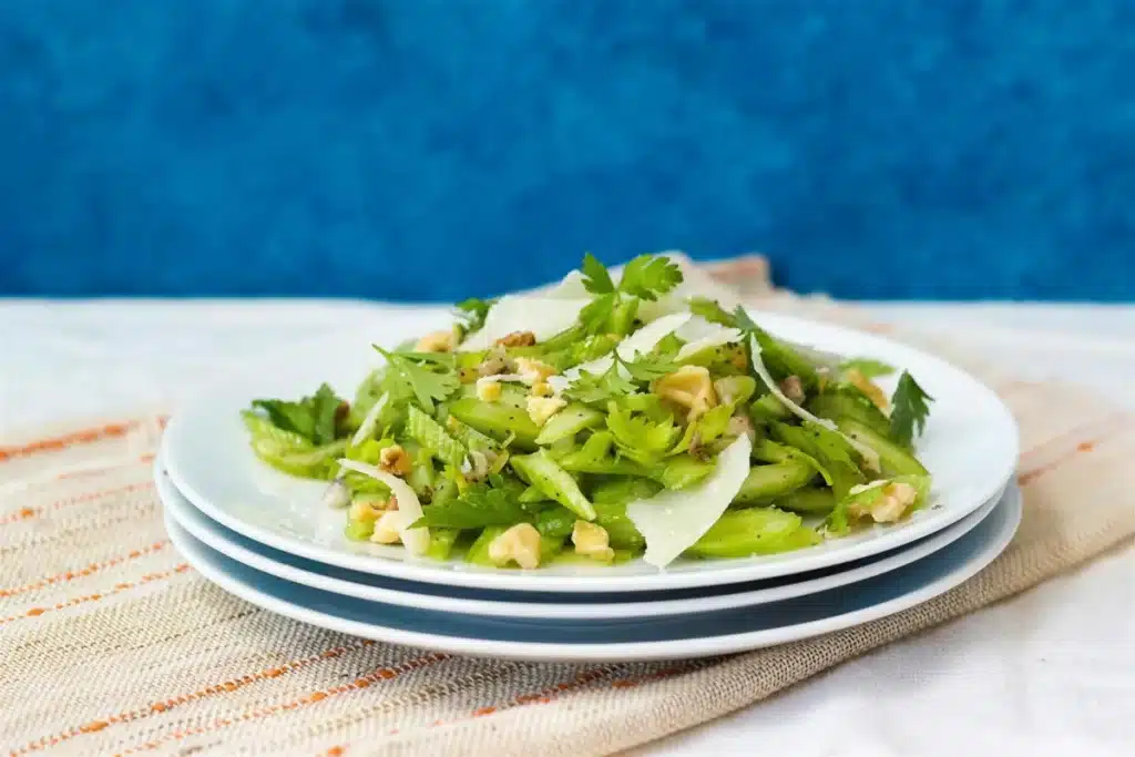 Celery salad with shaved parmesan and walnuts on stacked white plates