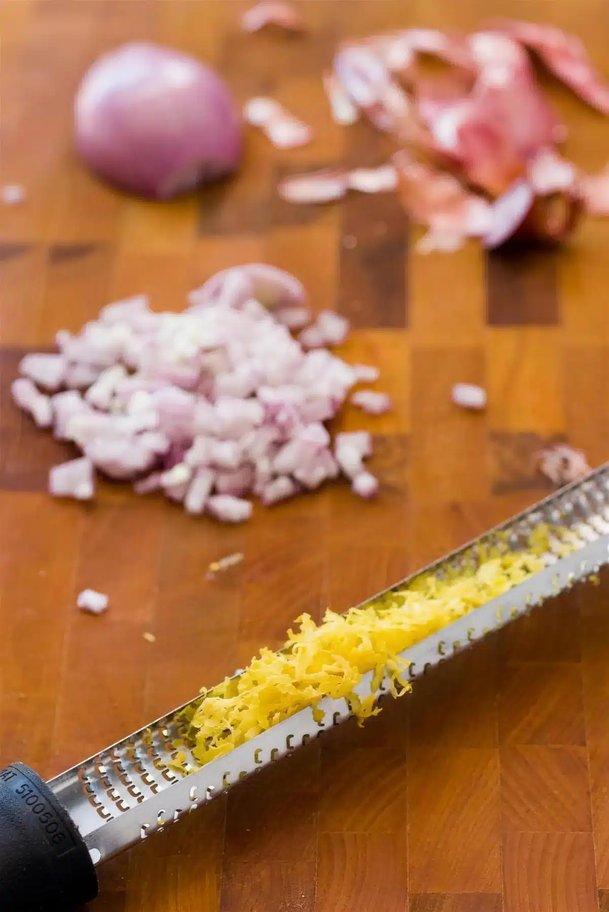 Minced shallot and lemon zest on a wooden board beside a microplane