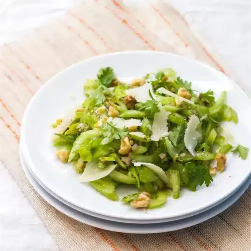 Celery salad on stacked white plates with shaved parmesan and toasted walnuts