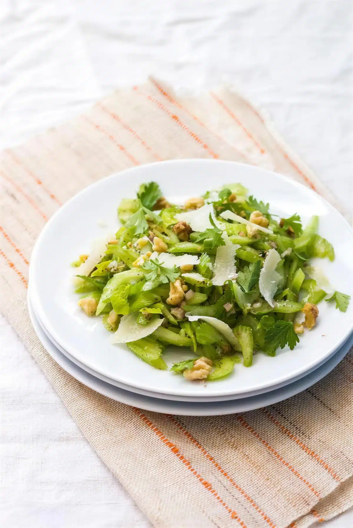 Celery salad on stacked white plates with shaved parmesan and toasted walnuts