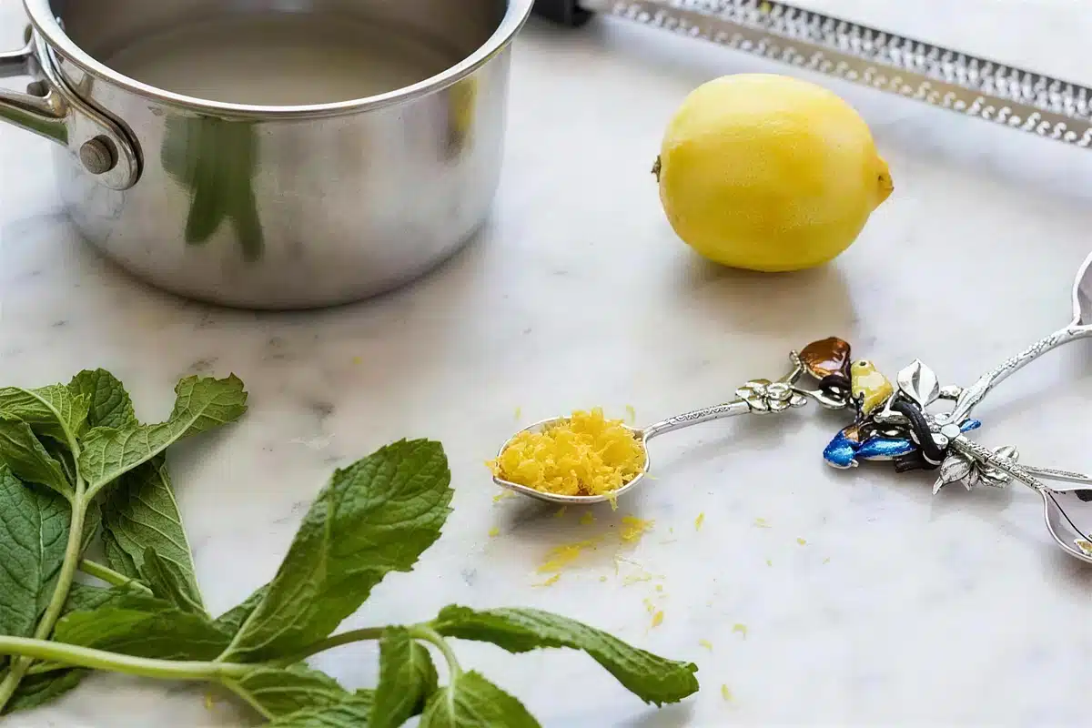 Mint leaves, a lemon and a small pot on a marble counter