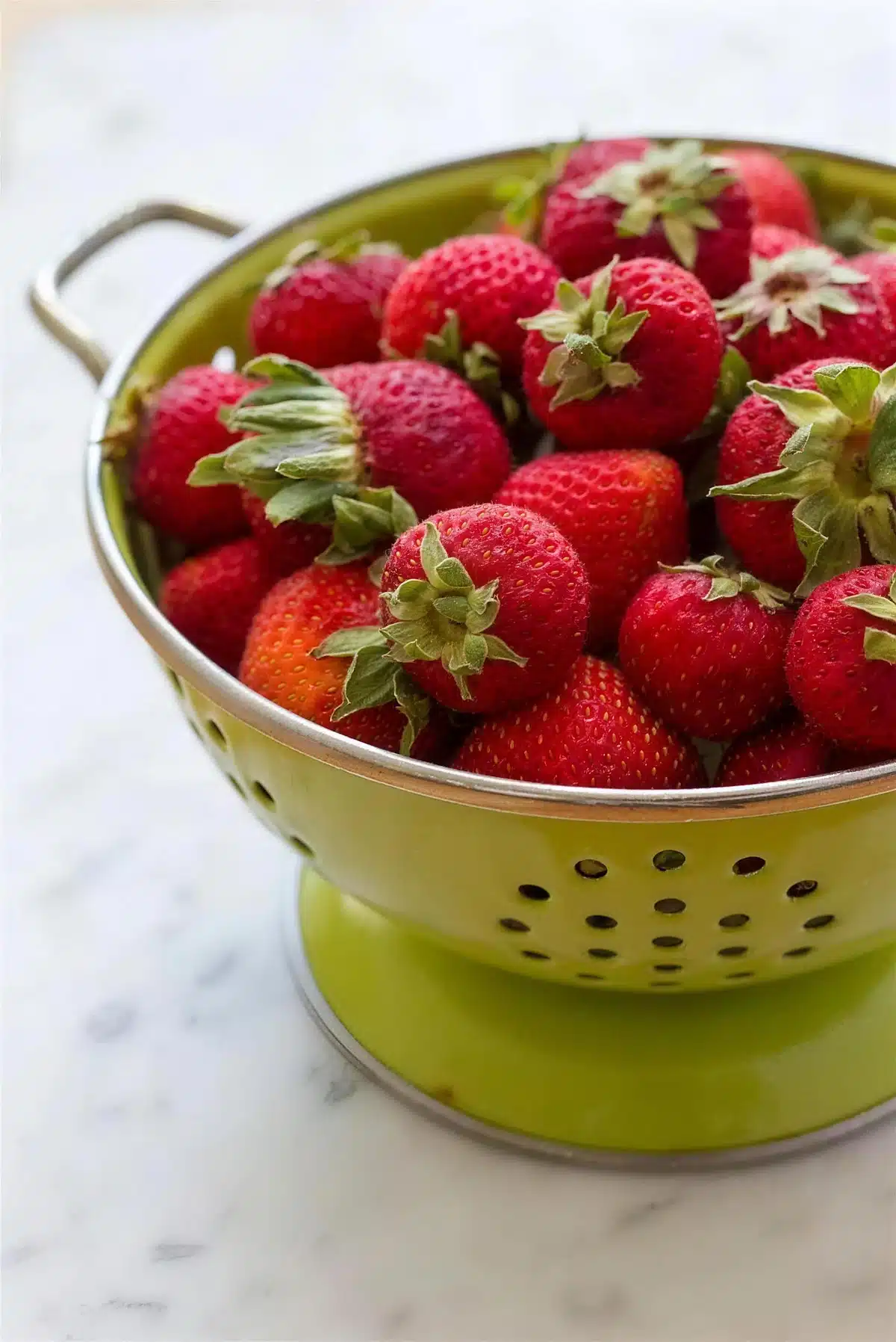 Fresh hulled berries piled in a green colander