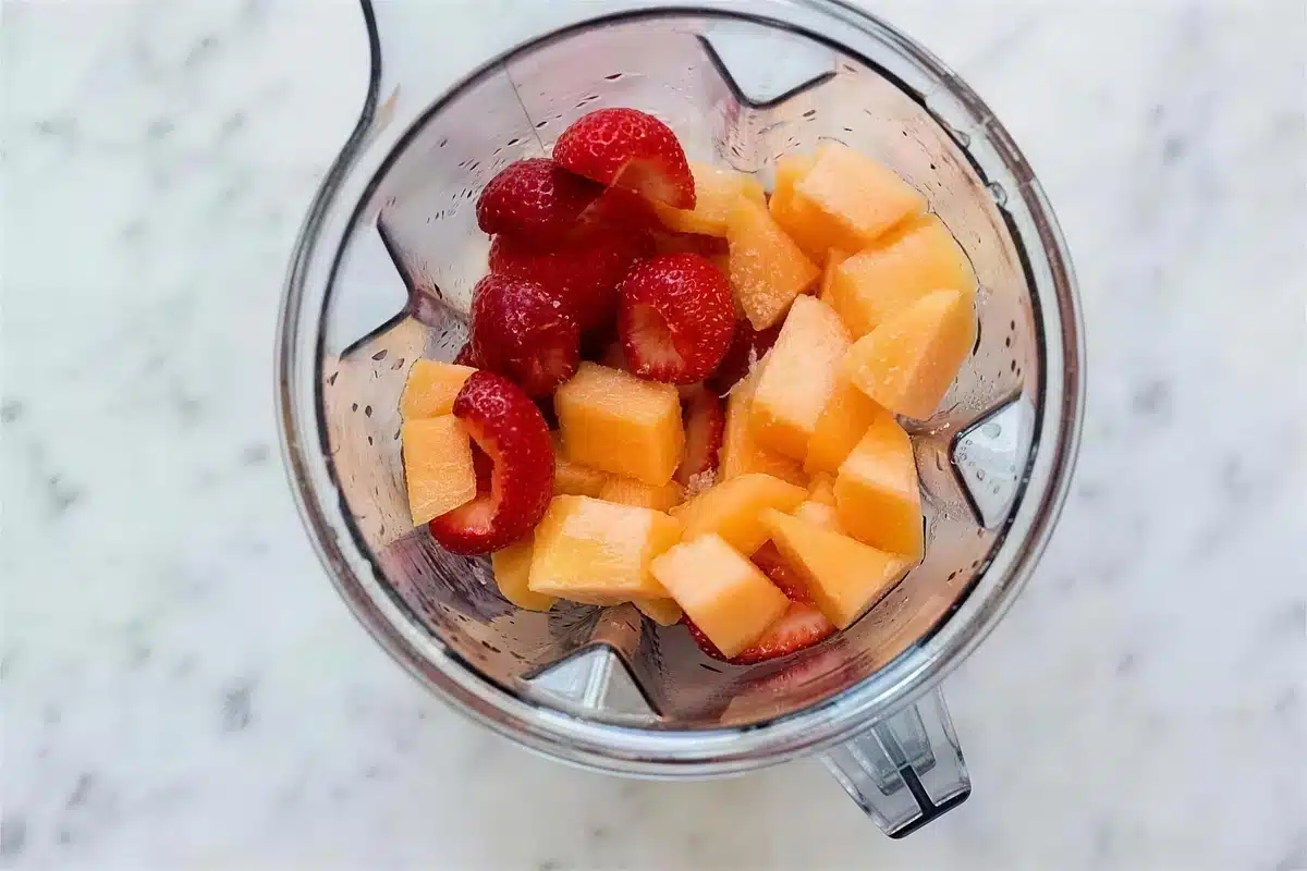 Strawberry sorbet base being blended with cubes of melon in a blender jar