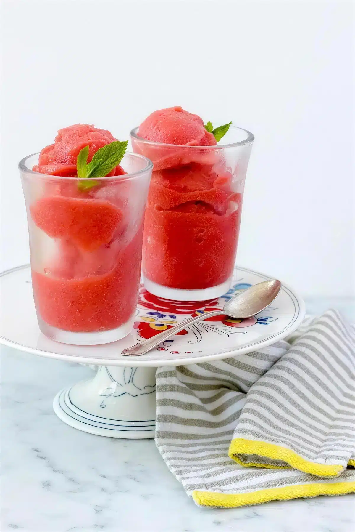 Strawberry sorbet in two glasses with mint leaves on a floral plate