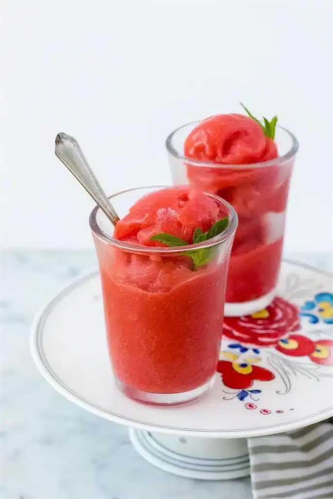 Two glasses of pale pink frozen dessert with spoons on a striped cloth