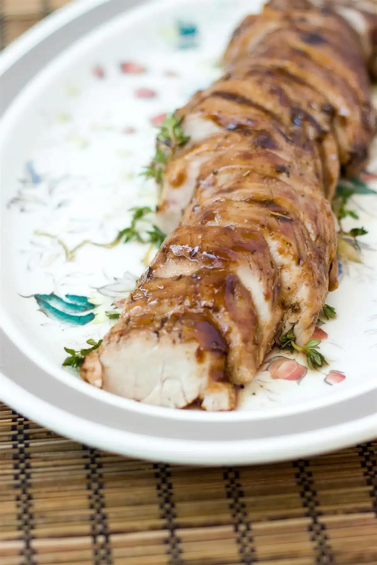 Balsamic pork tenderloin sliced into thick rounds on a floral platter
