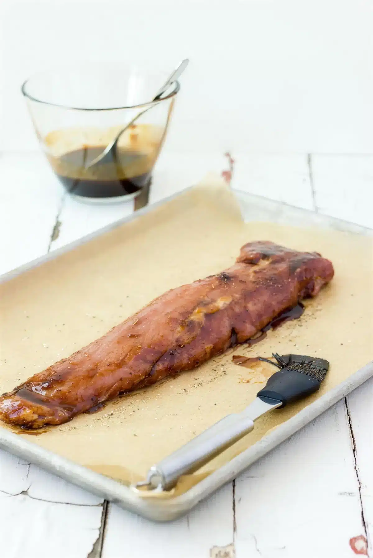 Balsamic pork tenderloin on a lined sheet pan being brushed with apricot glaze