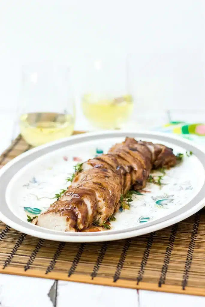 Whole glazed pork tenderloin resting on a floral platter