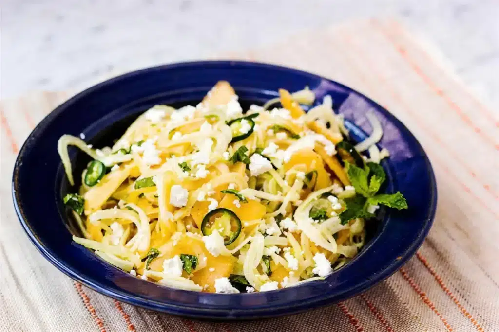 Thin white and orange ribbons with feta and mint in a blue bowl