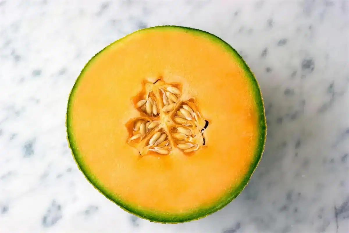 A halved cantaloupe cut side up on white marble