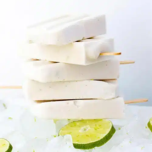 Coconut popsicles stacked on crushed ice with lime slices around them