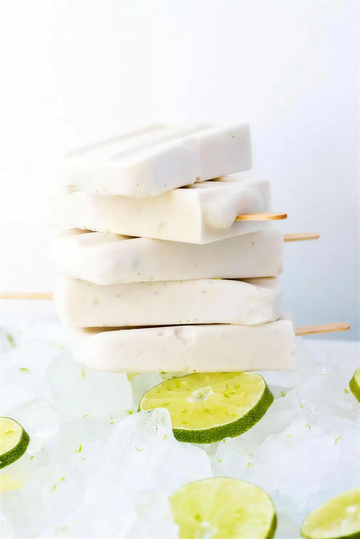 Coconut popsicles stacked on crushed ice with lime slices around them