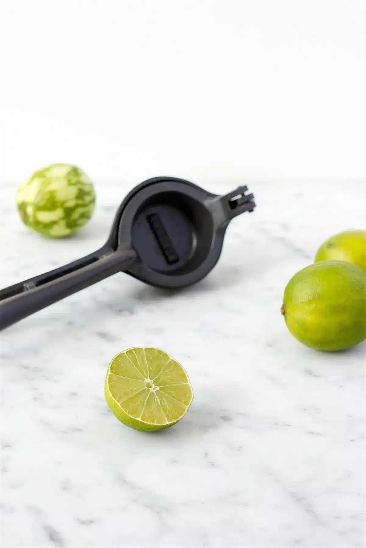 Halved limes and a hand squeezer on a marble counter