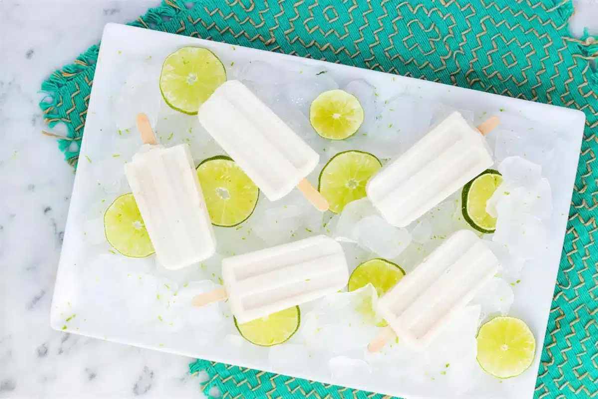 Coconut popsicles laid out on a white tray of crushed ice over a teal mat