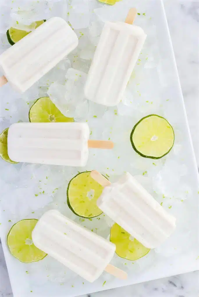 White ice pops on wooden sticks arranged over crushed ice with citrus slices