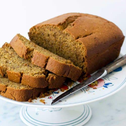 Pumpkin beer bread sliced on a china cake stand with a serrated knife