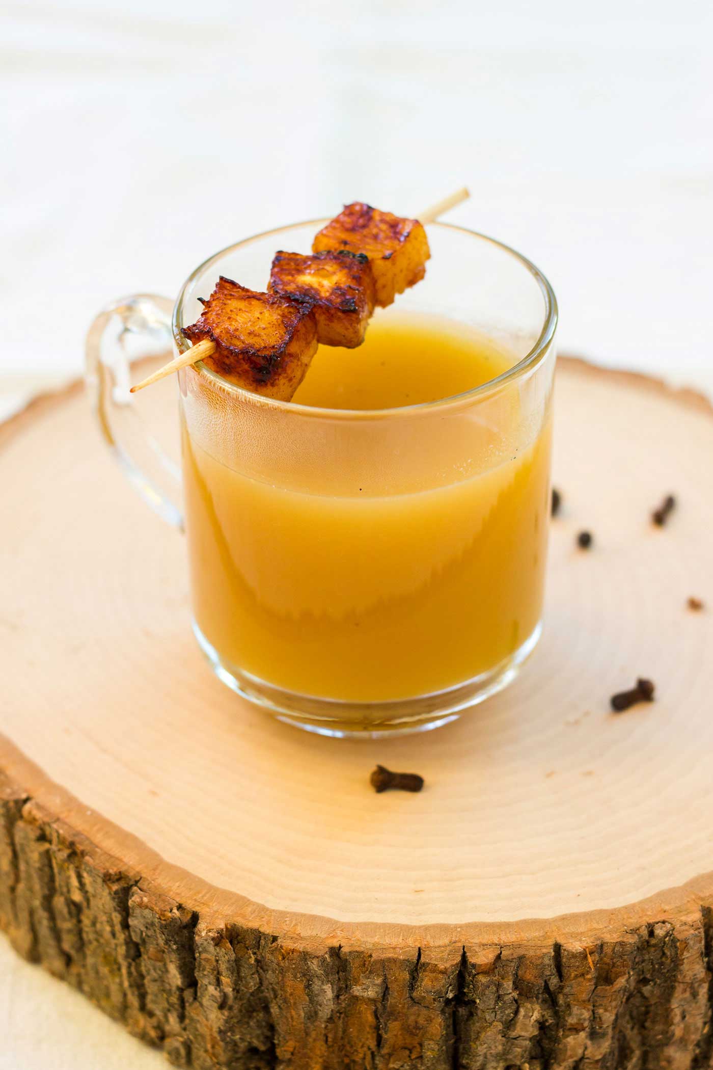 A single glass mug of hot golden drink on a birch slice with cloves scattered around it