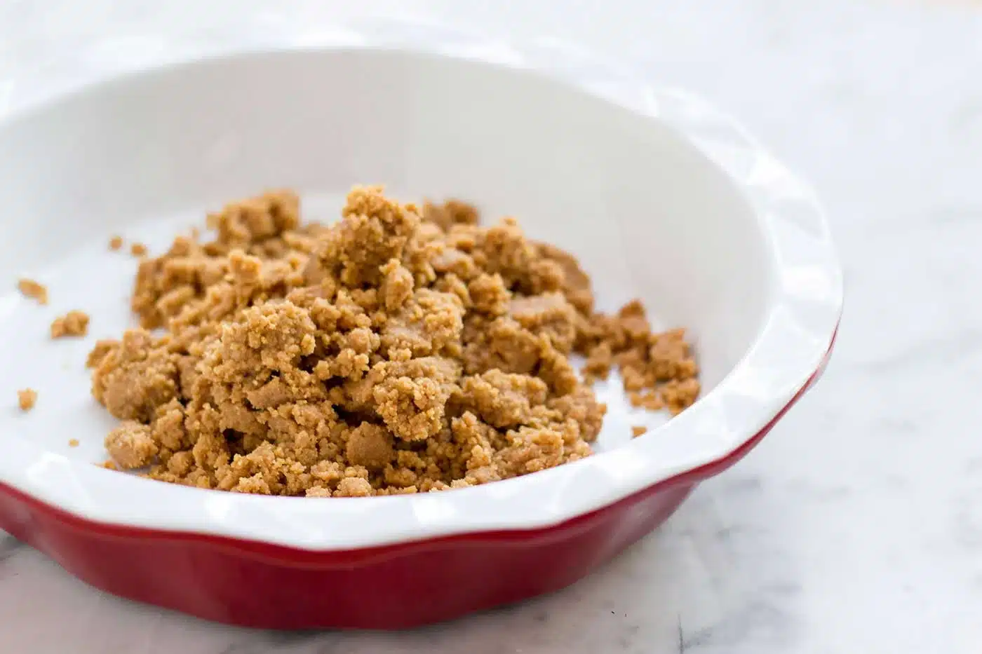 Pressed crumb crust in a fluted red and white dish before baking