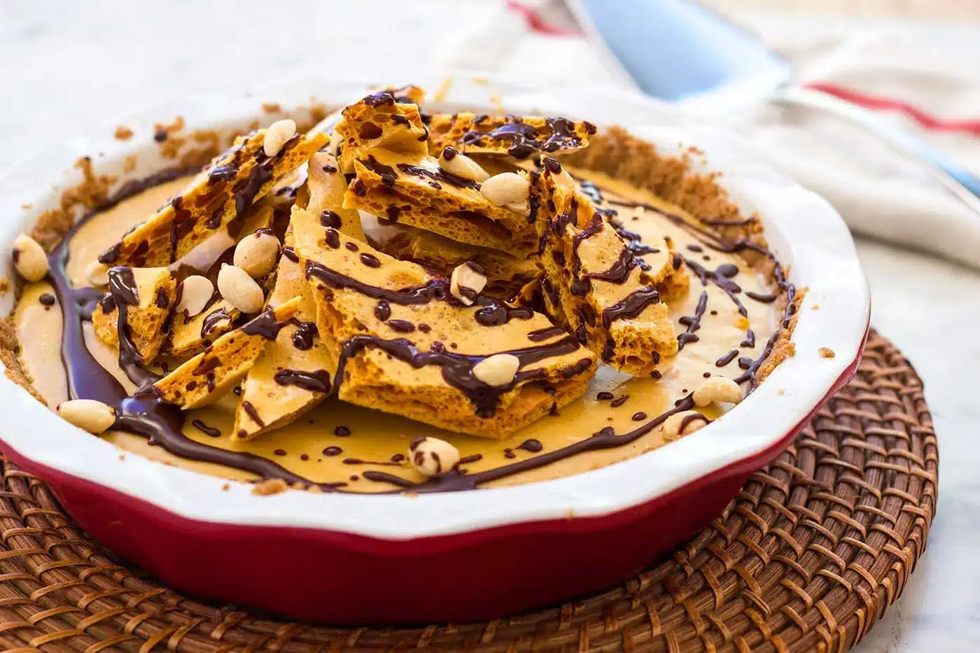 Whole peanut butter cream pie in a red dish under a pile of honeycomb and chocolate