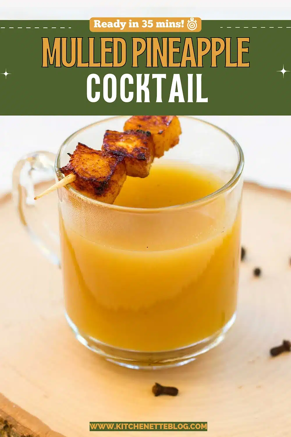 A glass mug of hot golden drink with a caramelized fruit skewer resting on a wood slice