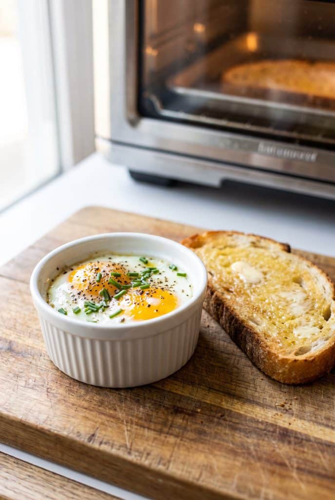 Baked eggs in a white ramekin with buttered toast on a wooden board