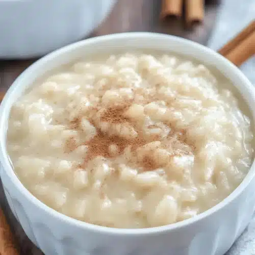 Slow cooker rice pudding dusted with cinnamon in a fluted white bowl