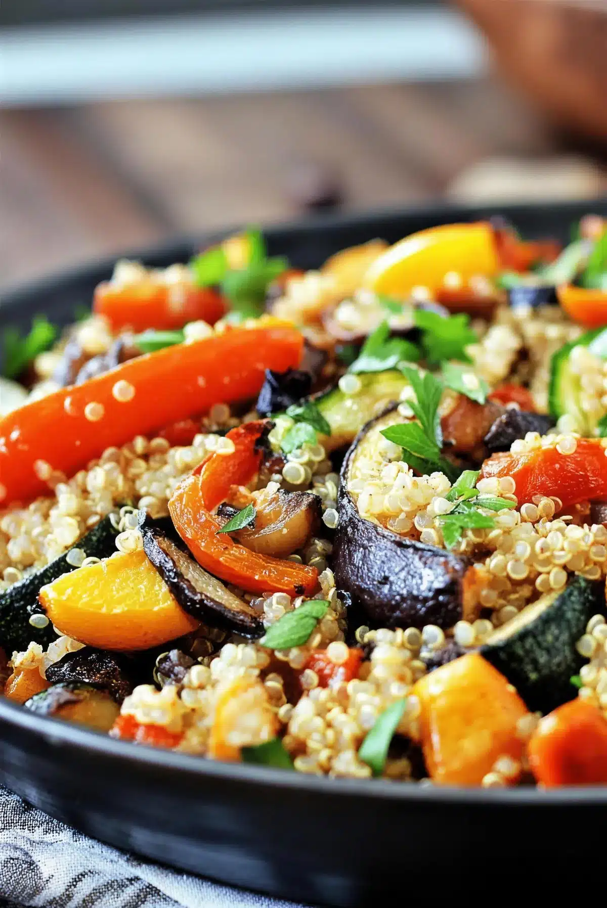 Dark bowl of grains, eggplant, carrot and yellow squash on wood