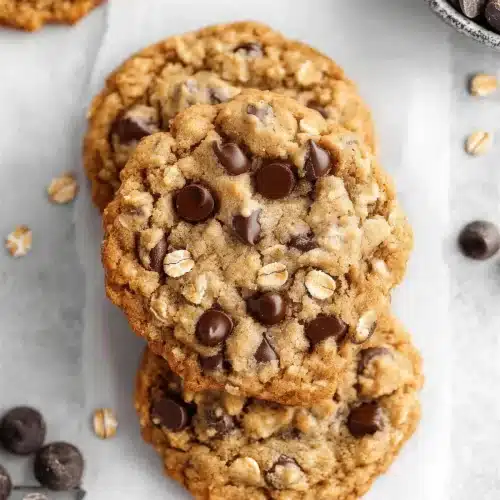 Vegan oatmeal chocolate chip cookies cooling on parchment beside a bowl of chips