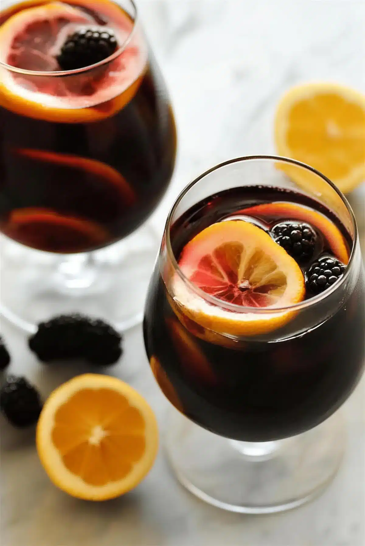Blackberry sangria in two glasses with a lemon wheel and a halved orange
