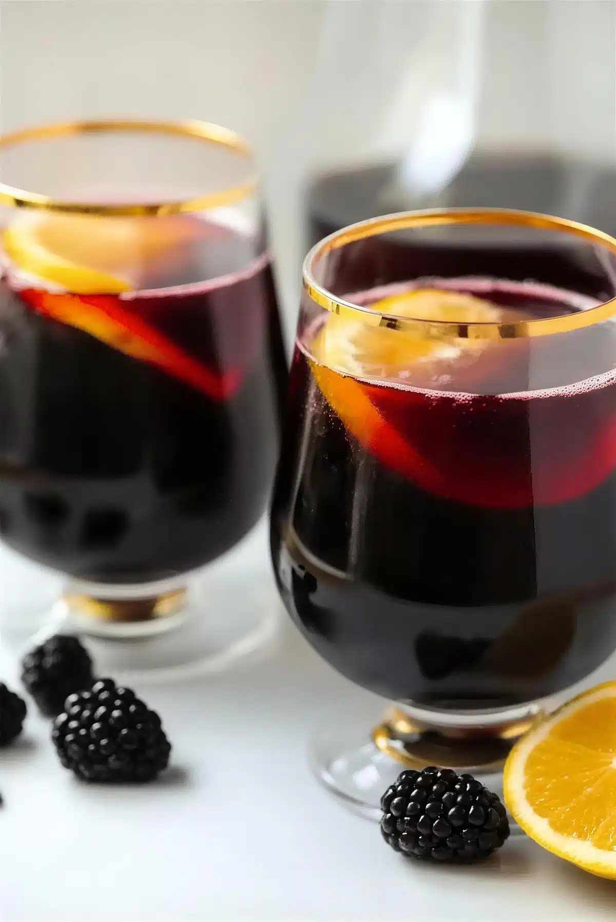 A pitcher and two gold-rimmed glasses of dark red wine punch