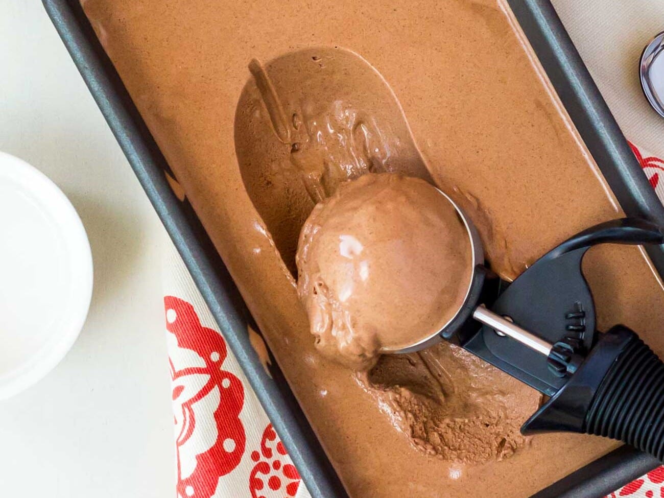 Metal scoop lifting a ball of ice cream out of a chilled pan