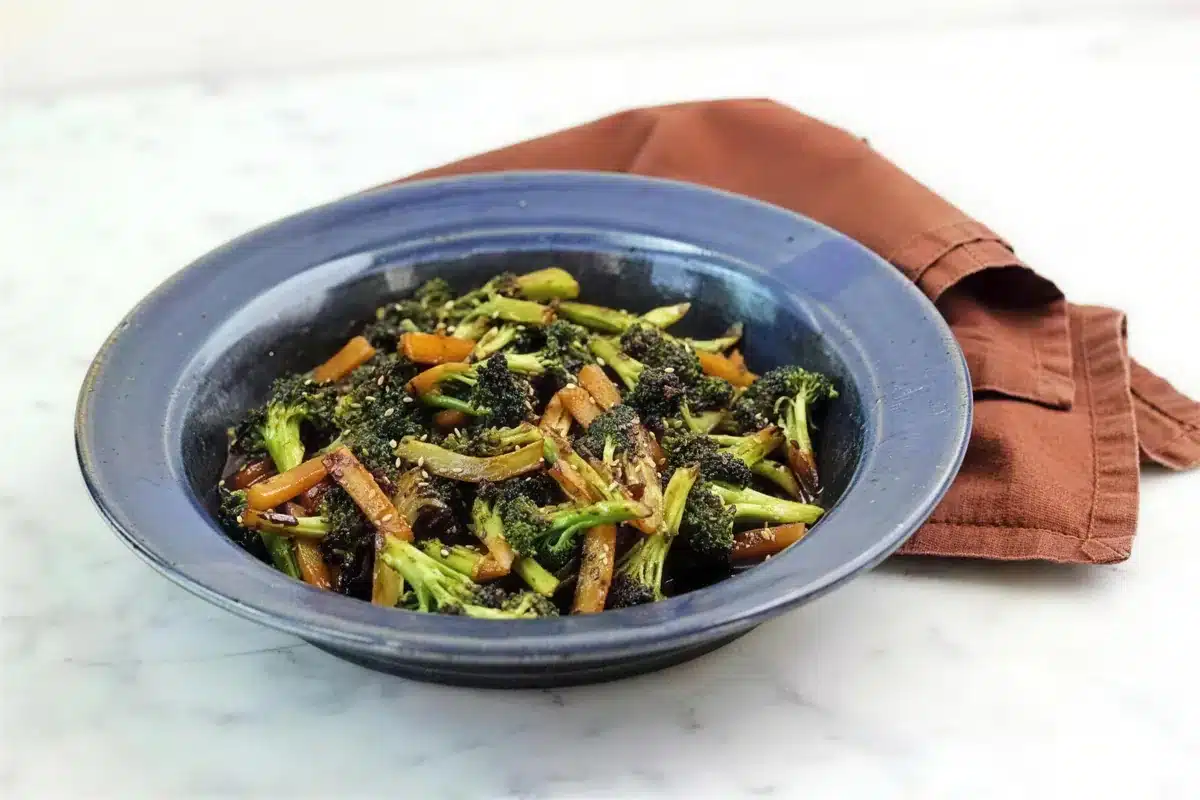 Asian broccoli piled in a blue ceramic bowl with a rust linen napkin behind