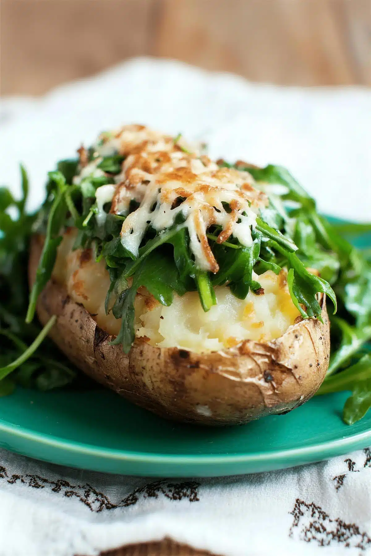 Close view of a split baked potato under wilted greens and browned cheese