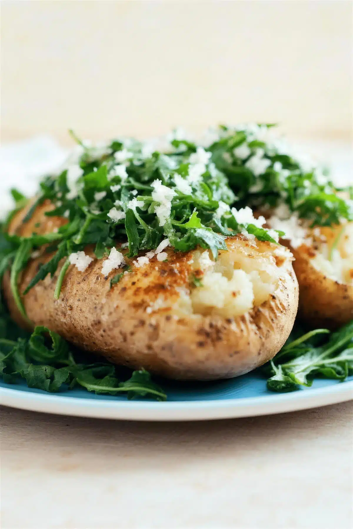 Sauteed arugula and parmesan over a fluffy baked potato on a green plate