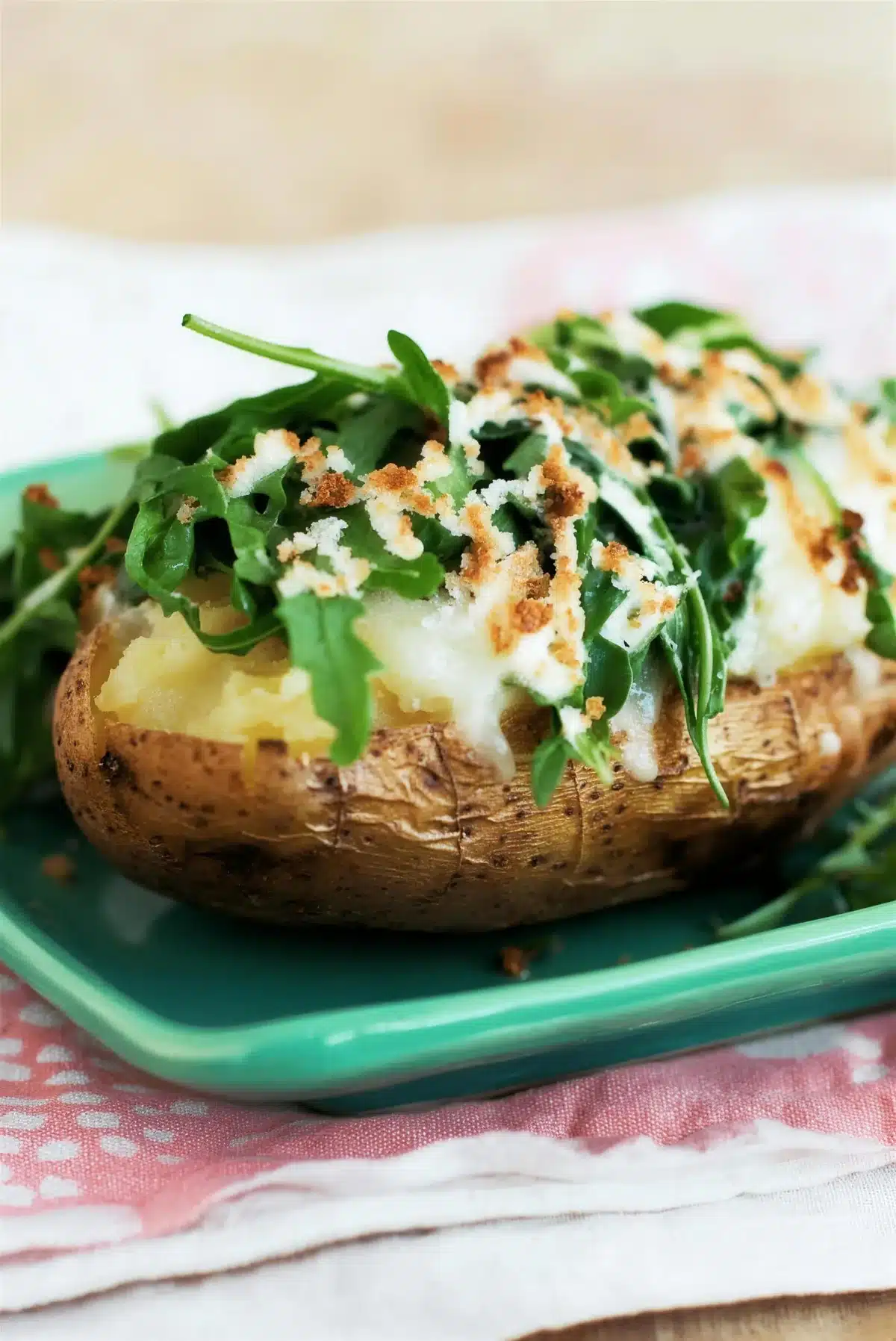 Sauteed arugula topping a baked potato on a pink cloth