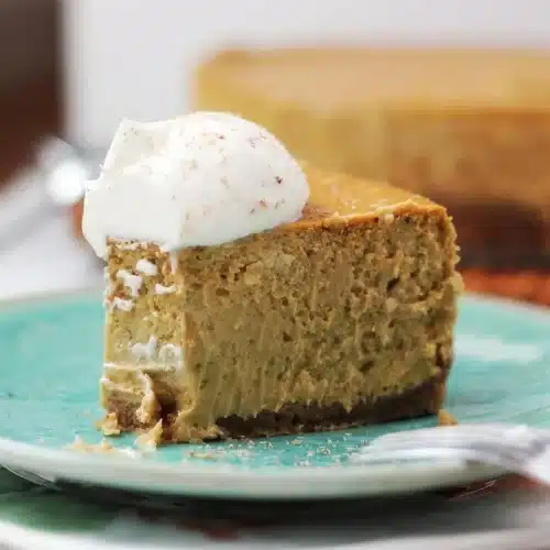A slice of pumpkin cheesecake and the whole cake behind it on a woven mat
