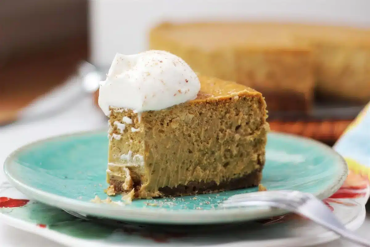 A slice of pumpkin cheesecake and the whole cake behind it on a woven mat