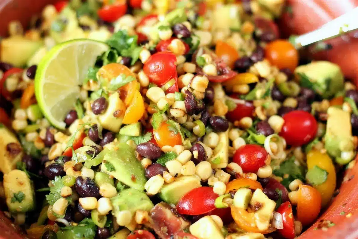 Close-up of charred corn salad with a lime wedge and cherry tomatoes