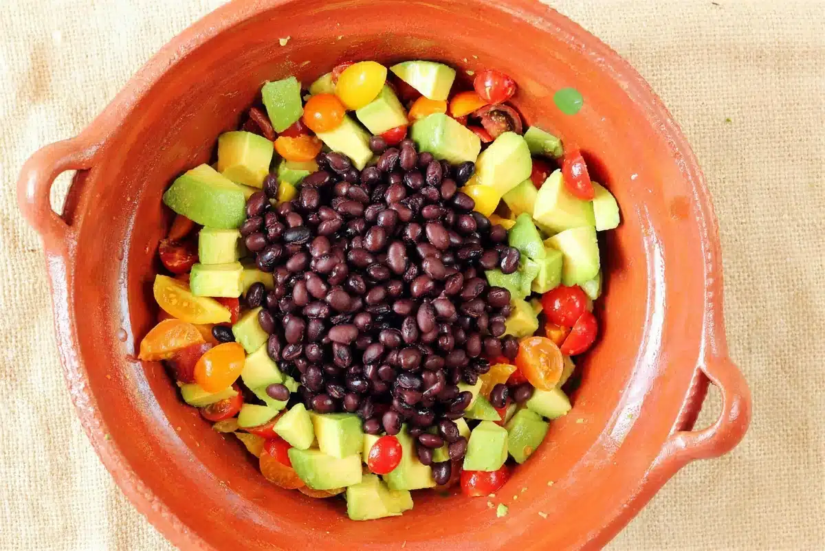 Black beans piled on diced avocado and tomatoes in a clay dish before tossing