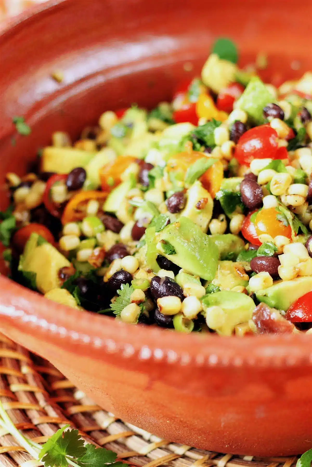Charred corn salad piled high in a terracotta bowl on a woven mat
