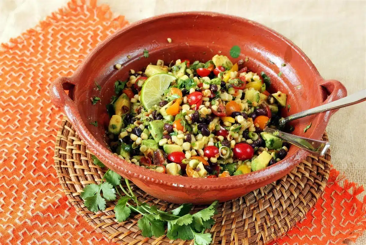 Charred corn salad in a clay dish with two forks on a woven mat
