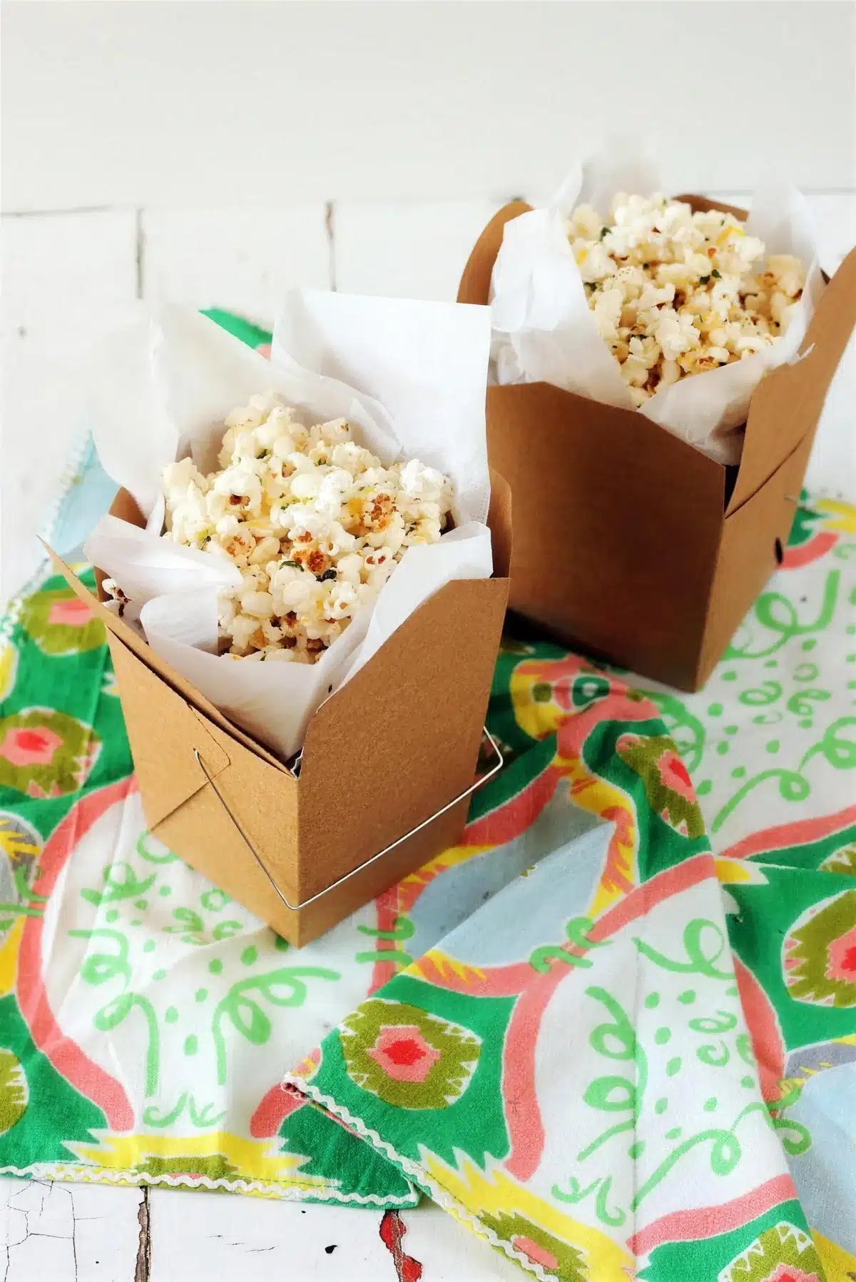 Homemade popcorn in two kraft cartons on a patterned green cloth