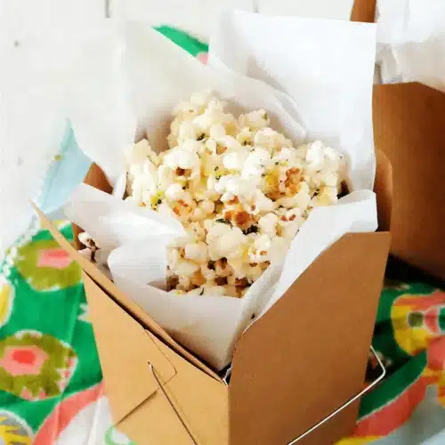 A carton of buttered popped corn lined with parchment on a green cloth