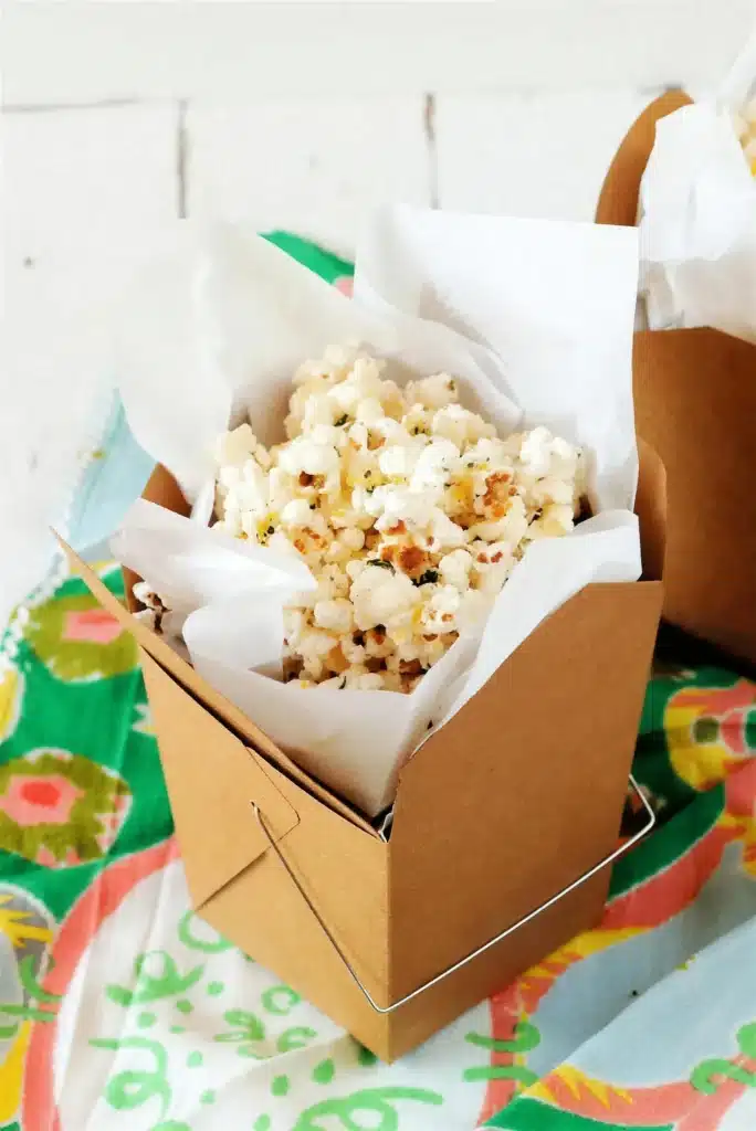 A carton of buttered popped corn lined with parchment on a green cloth