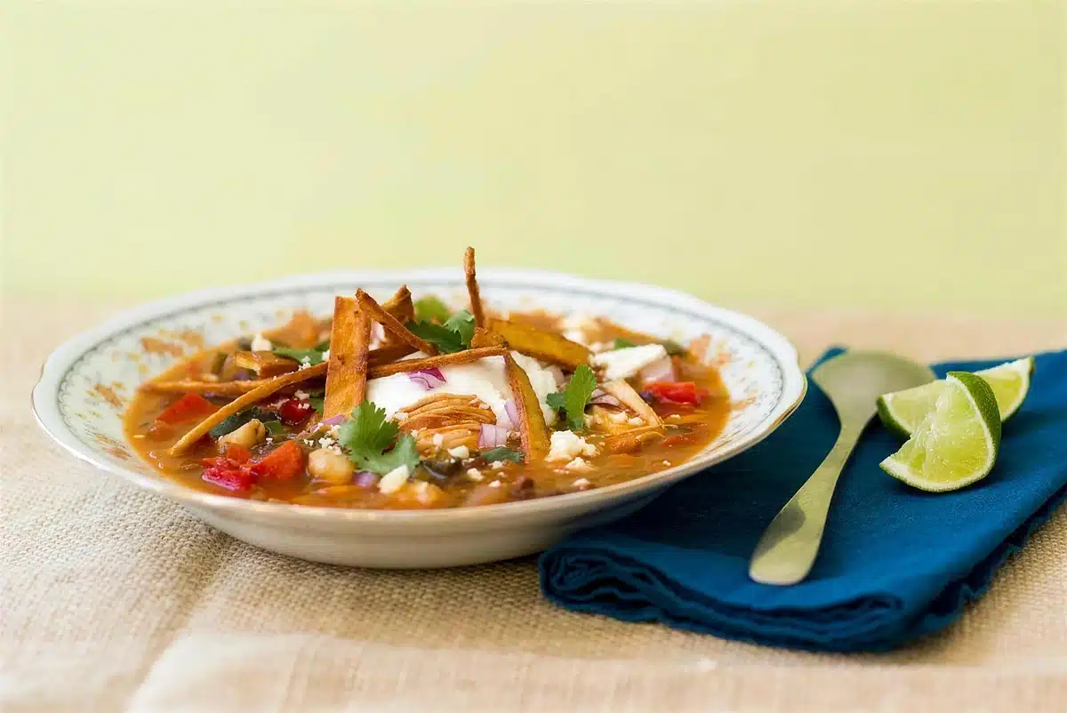 Chicken tortilla soup with lime wedges and a spoon set alongside
