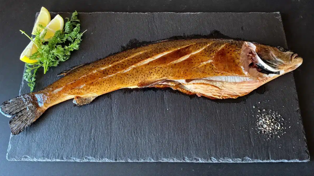 Smoked steelhead trout fillet with a glossy glaze and lemon wedges on slate