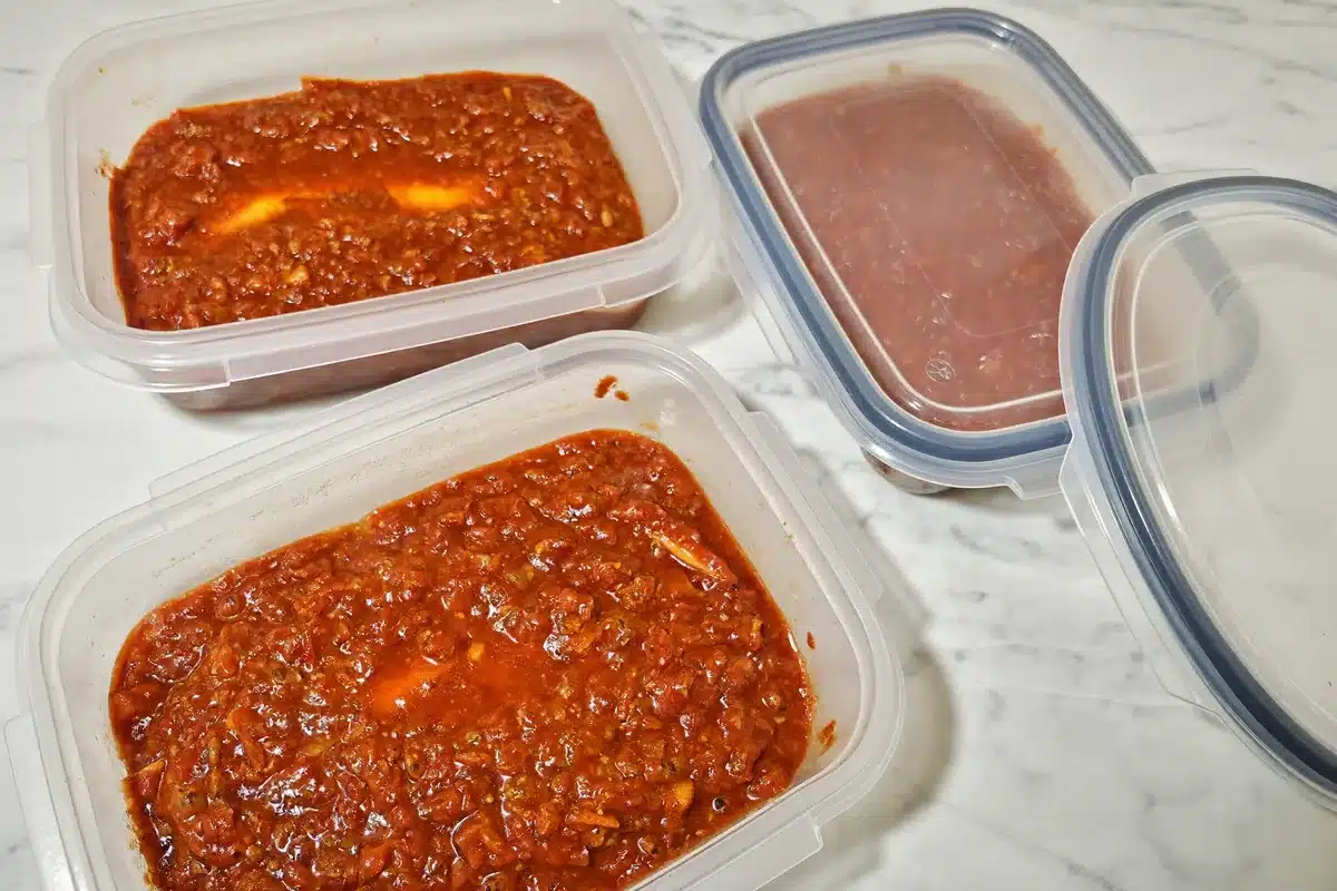 Portions of bolognese sauce in freezer-safe containers on a counter