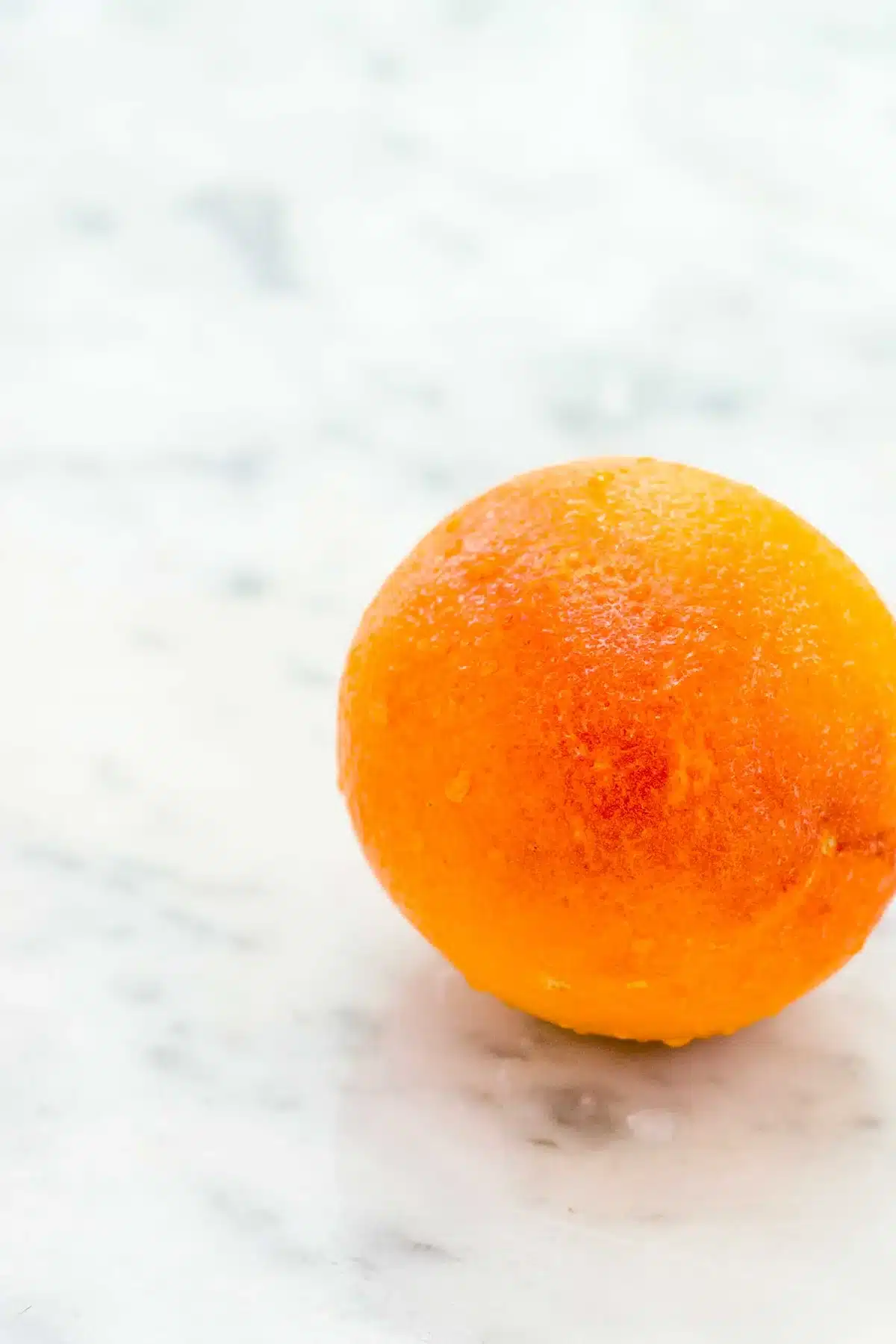 A single whole blood orange resting on a pale marble surface